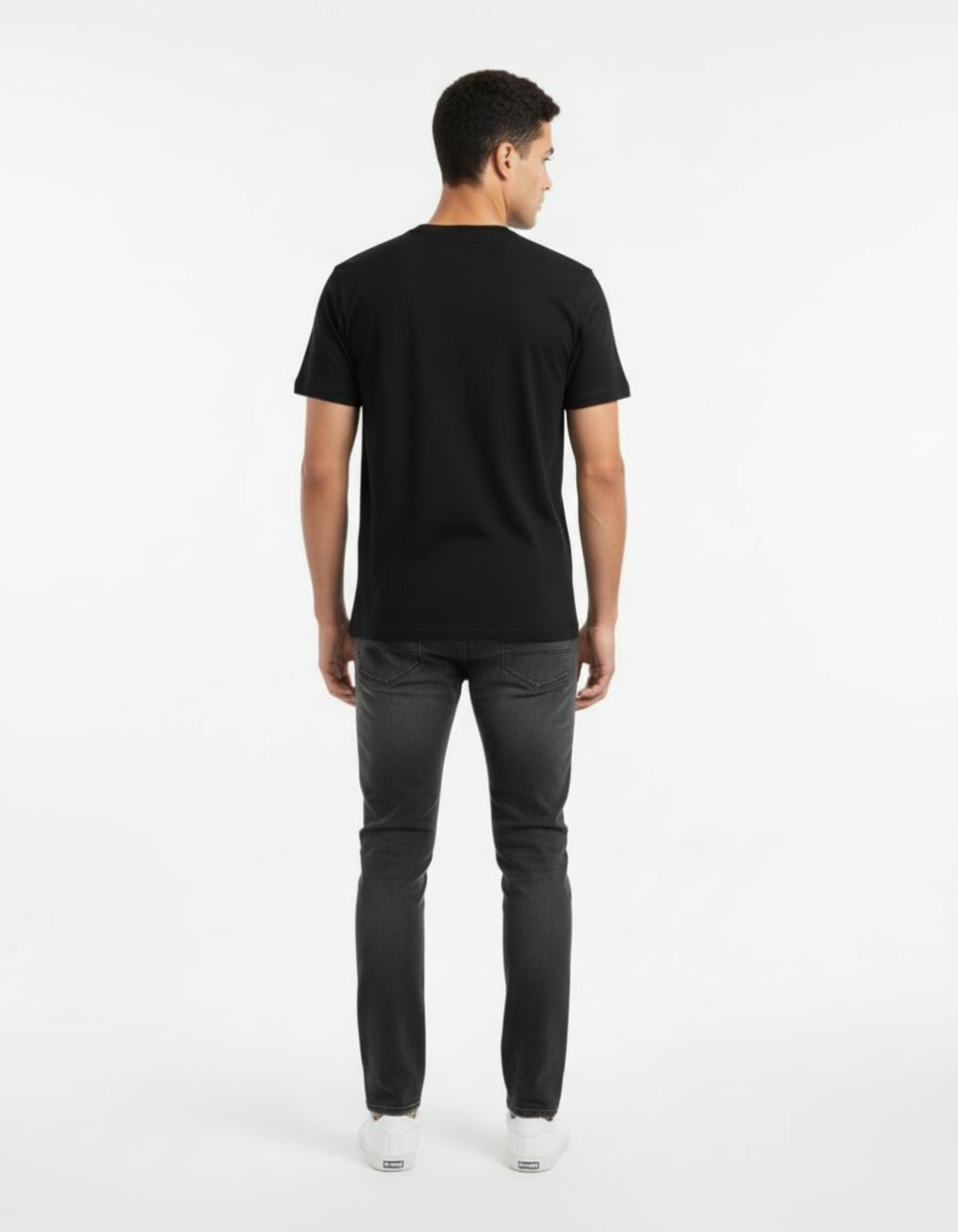 Man wearing a black t-shirt and dark jeans on a white background