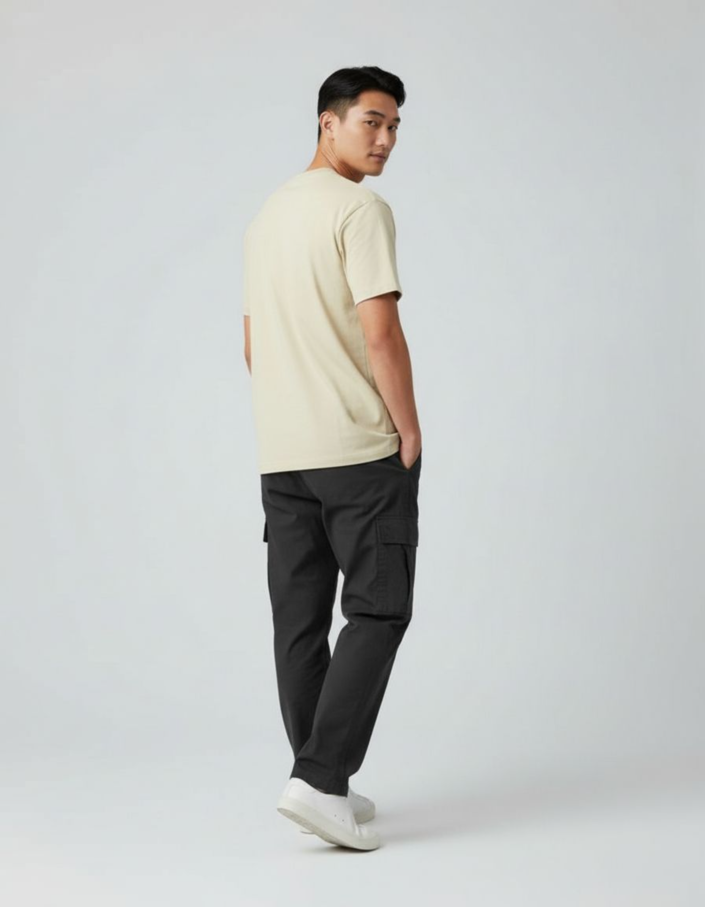 Man wearing a beige t-shirt and dark cargo pants on a white background