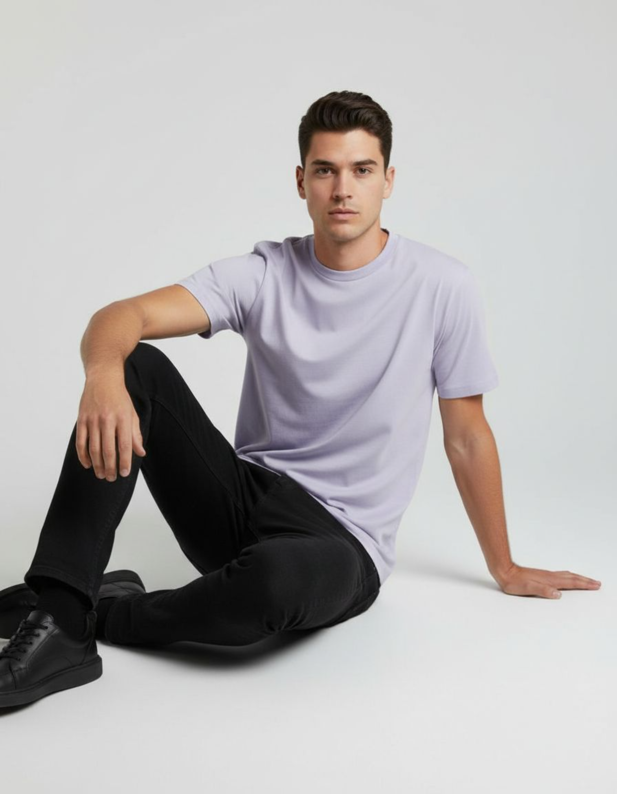 Man wearing a lavender t-shirt and black pants sitting on a white floor.