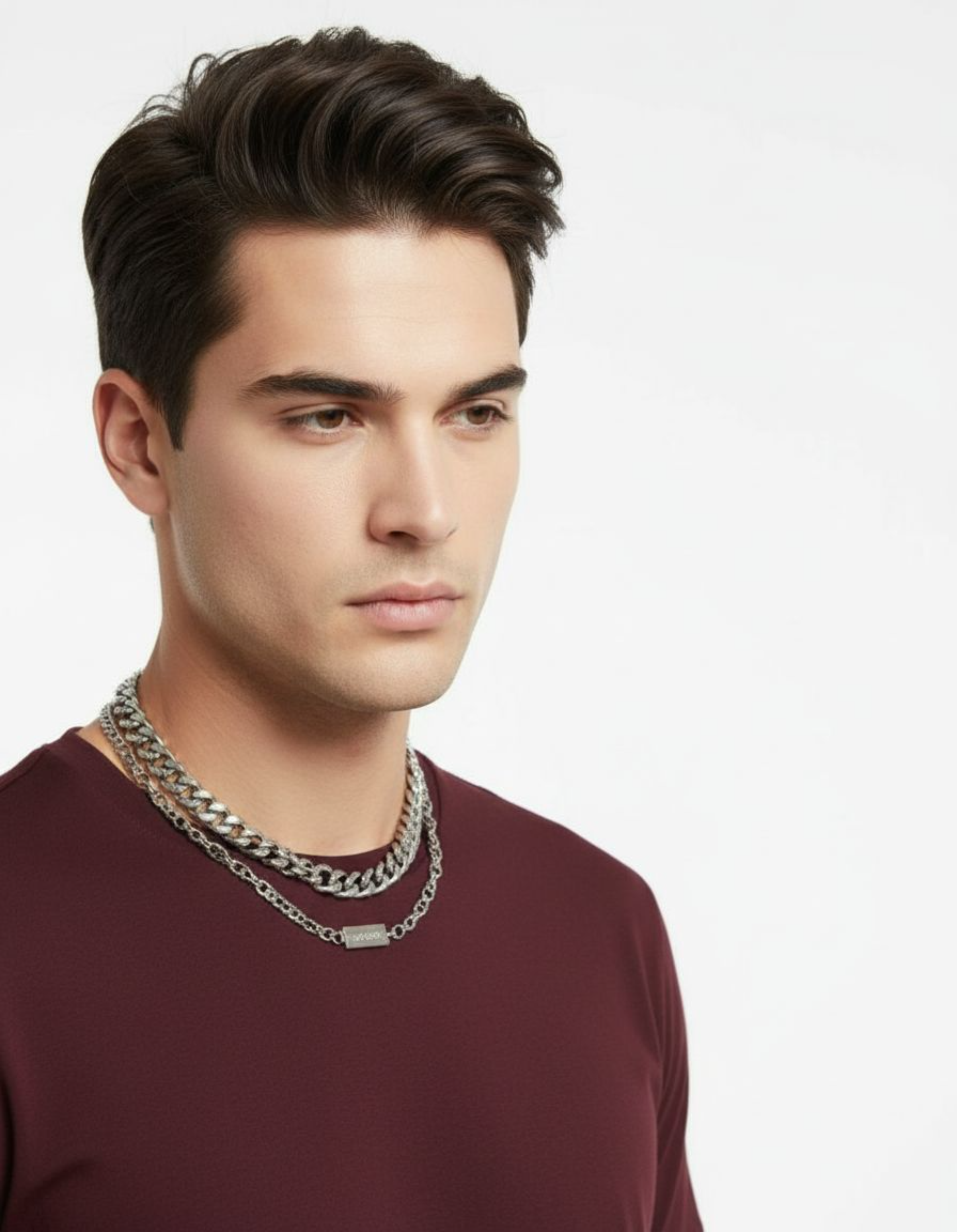 Man wearing a maroon shirt and multiple necklaces on a plain background