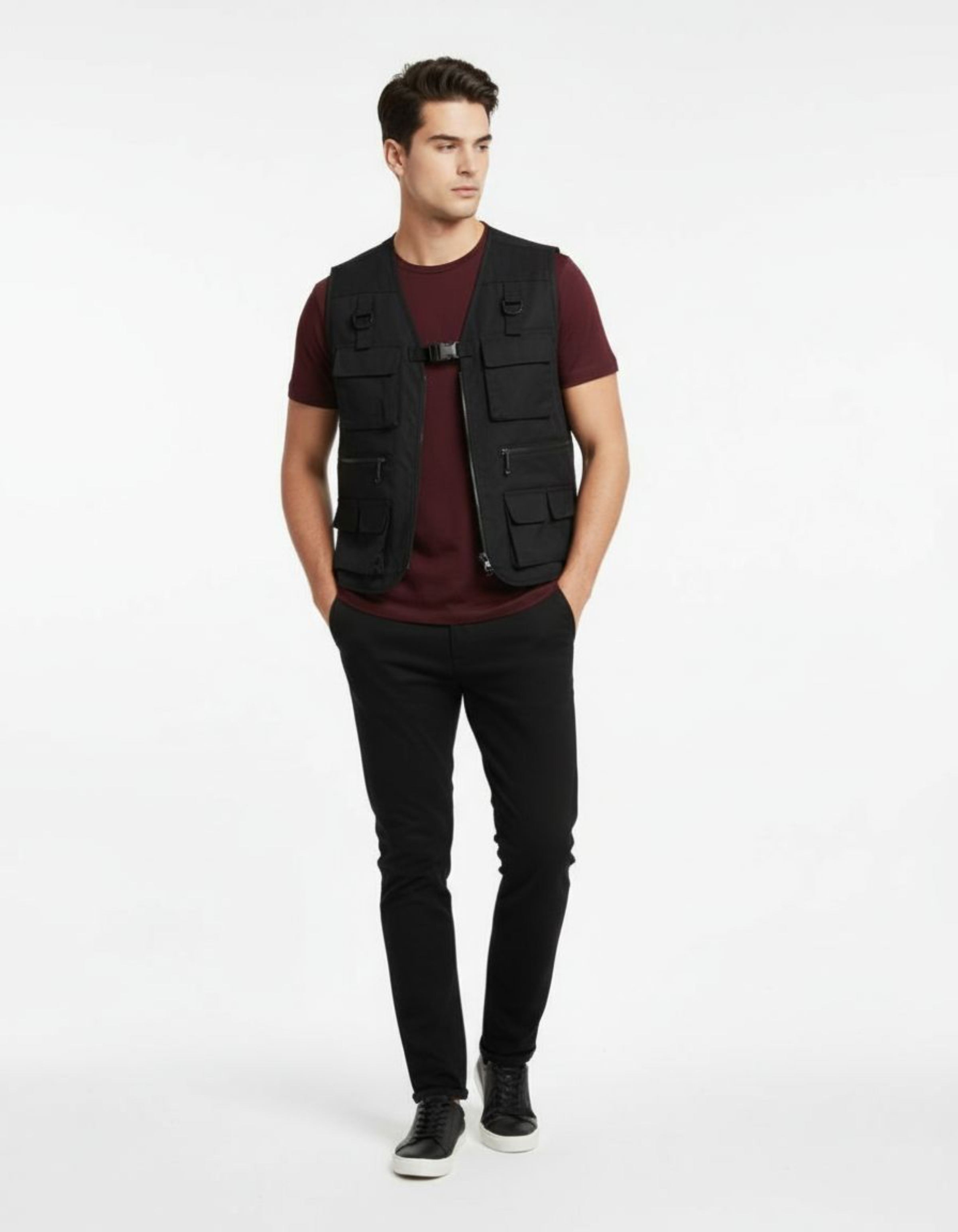 Man wearing a black vest over a maroon shirt with black pants on a white background