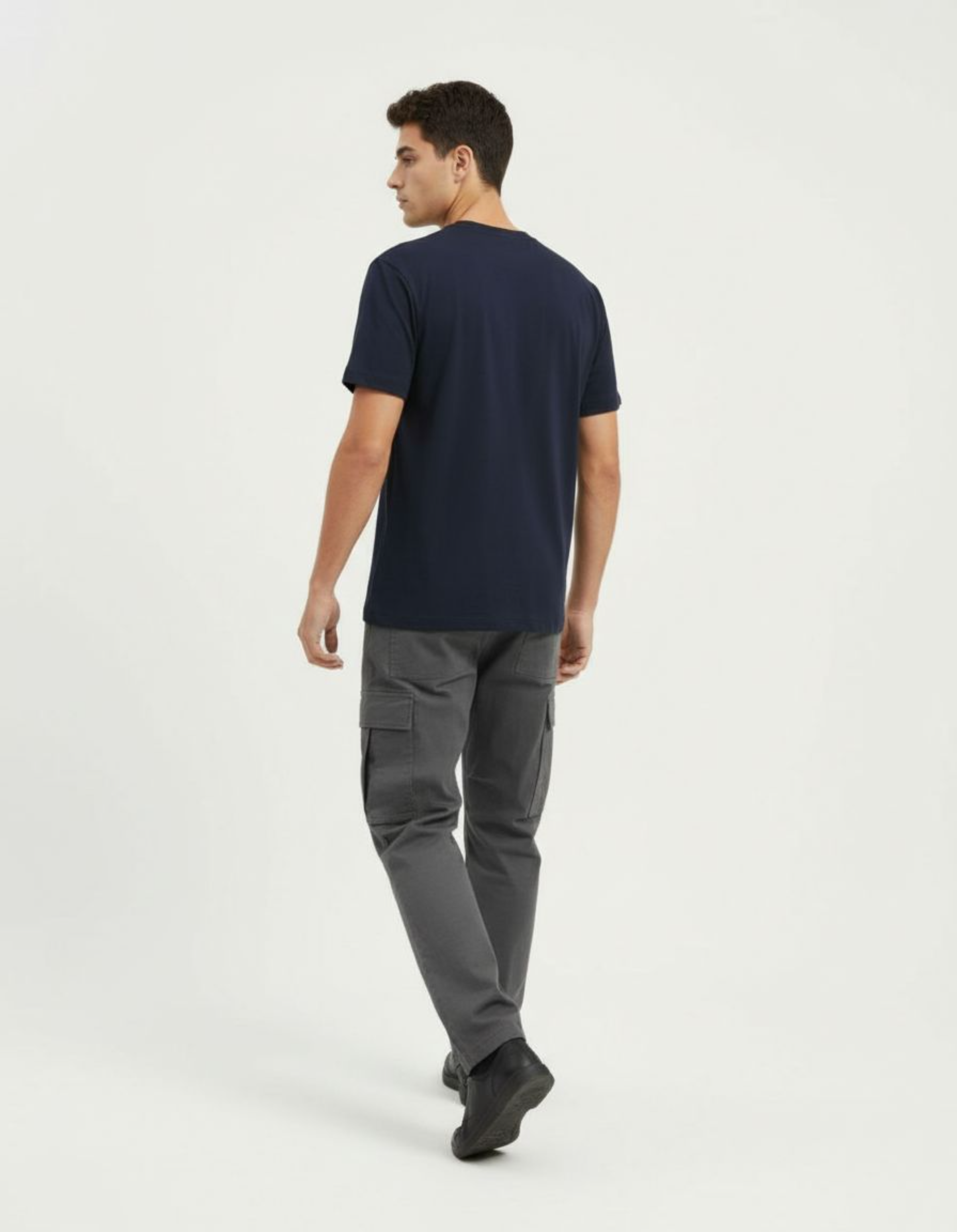 Man wearing a navy t-shirt and gray cargo pants on a white background