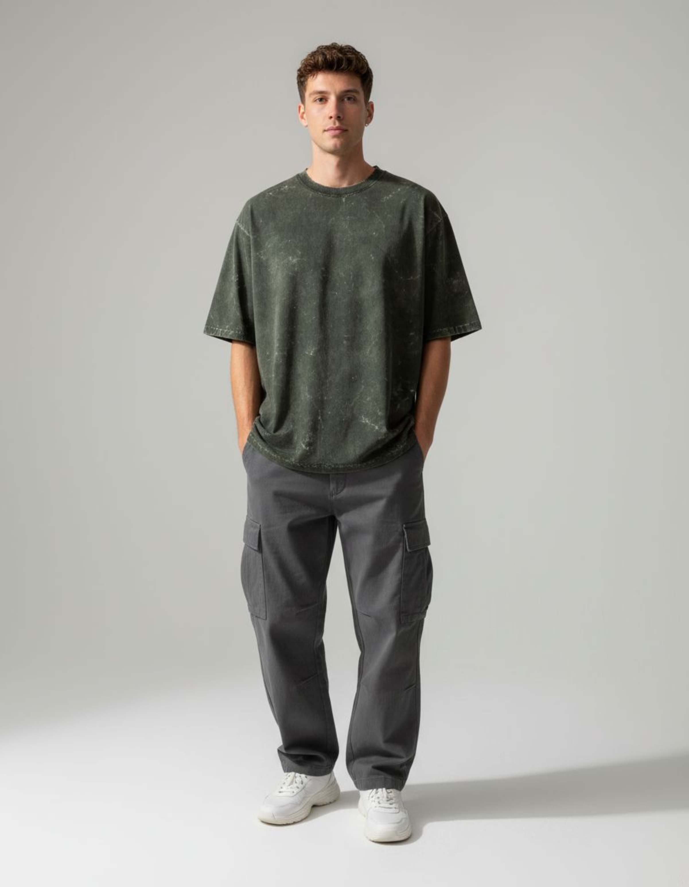 Man wearing an oversized olive green t-shirt and gray cargo pants on a plain background