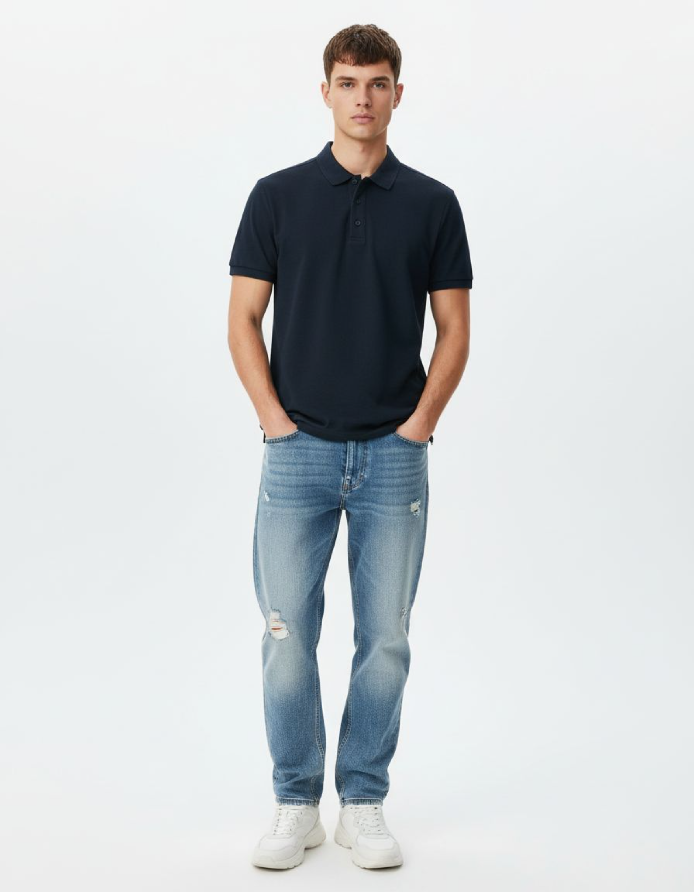 Man wearing a navy polo shirt and light blue jeans on a white background