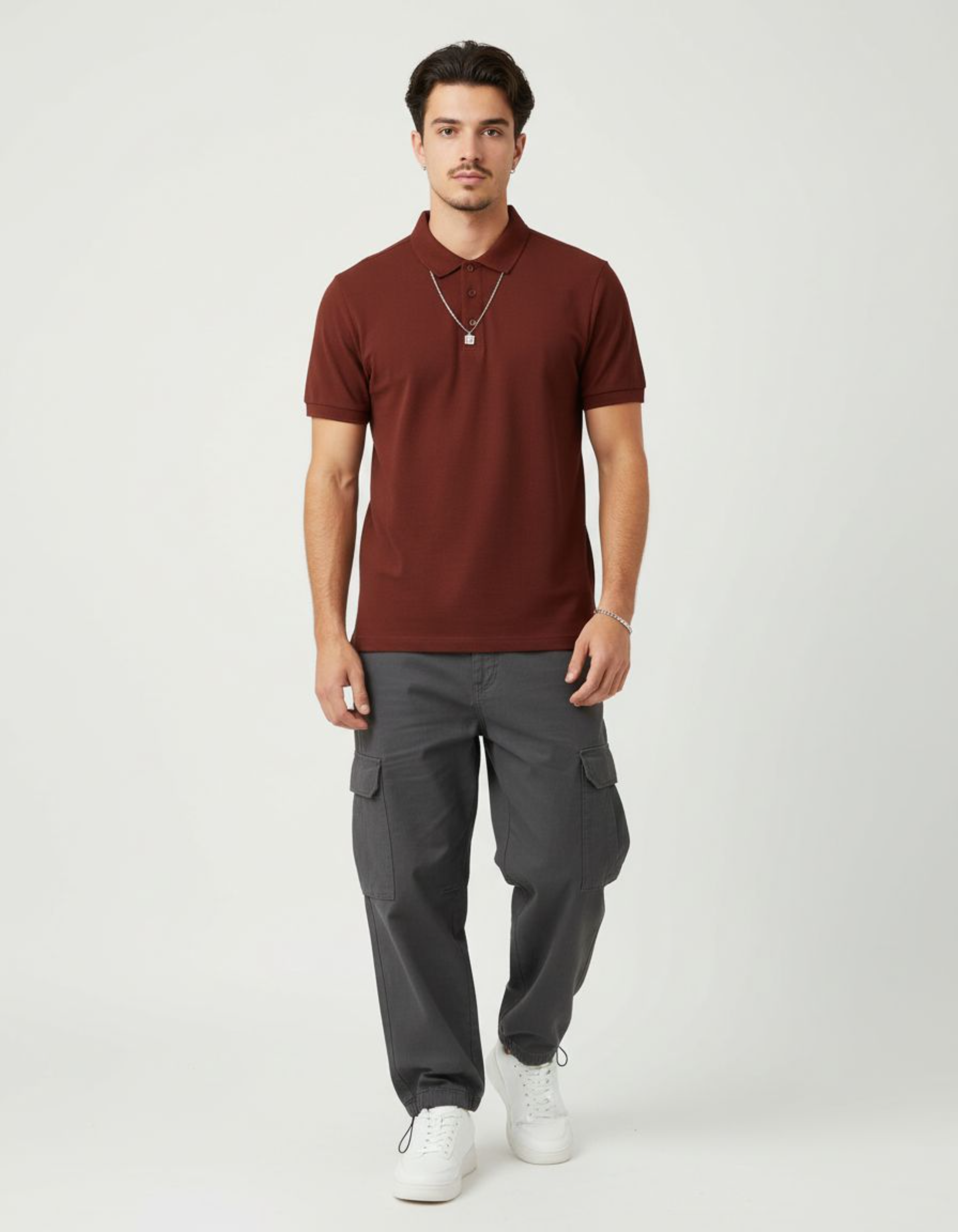 Man wearing a brick red polo shirt and gray cargo pants on a white background